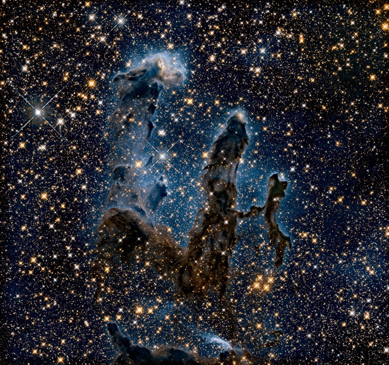 Vistos em infravermelho, técnica que nos permite perceber o que há por trás da maior parte da poeira, os Pilares da Criação mostram contornos mais delicados, com destaque para a "névoa" azul que contrasta com a poeira escura e a luz de inúmeras estrelas. Crédito: NASA/ ESA/Hubble/Hubble Heritage Team 