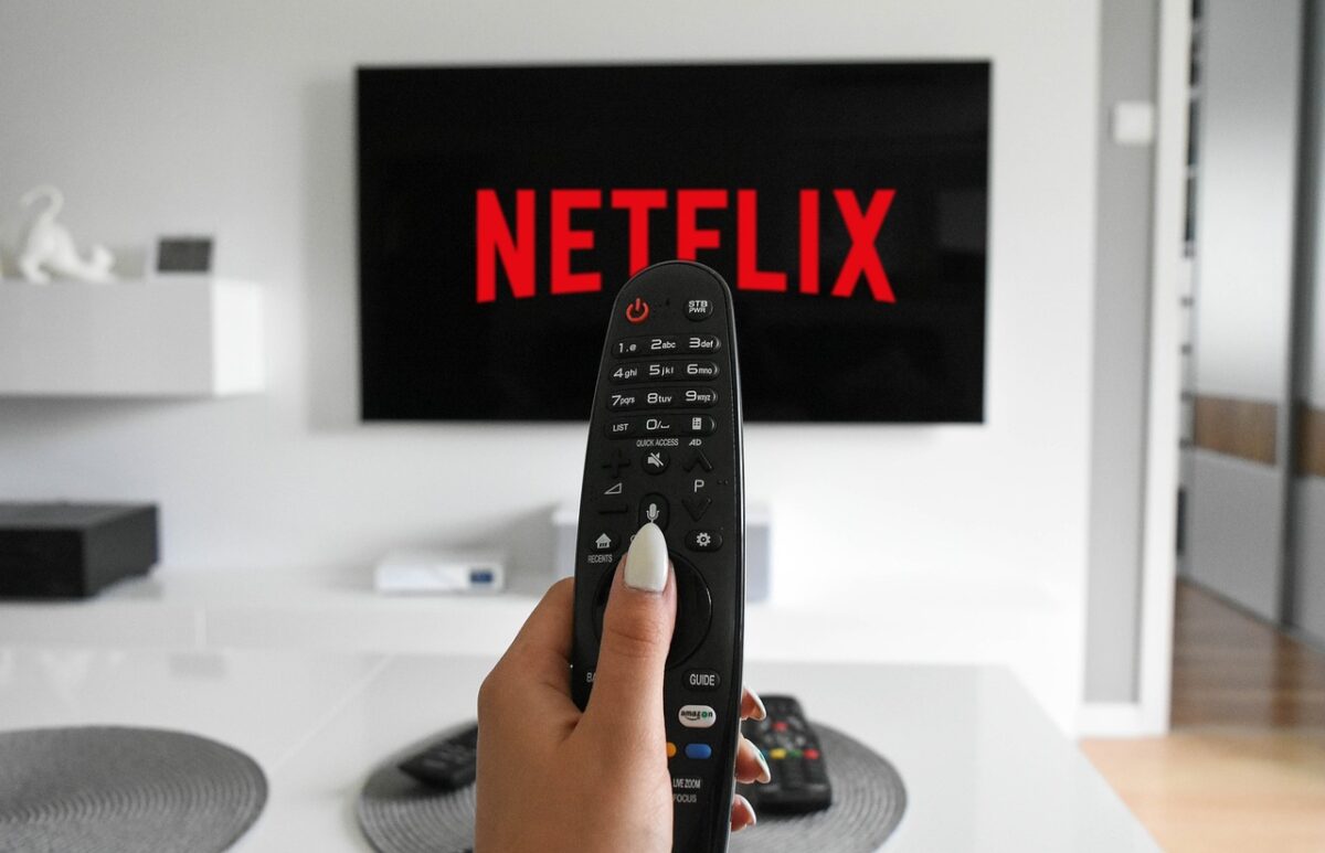 Mão com controle remoro e televisão ligada na Netflix