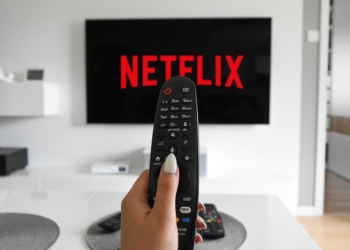 Mão com controle remoro e televisão ligada na netflix