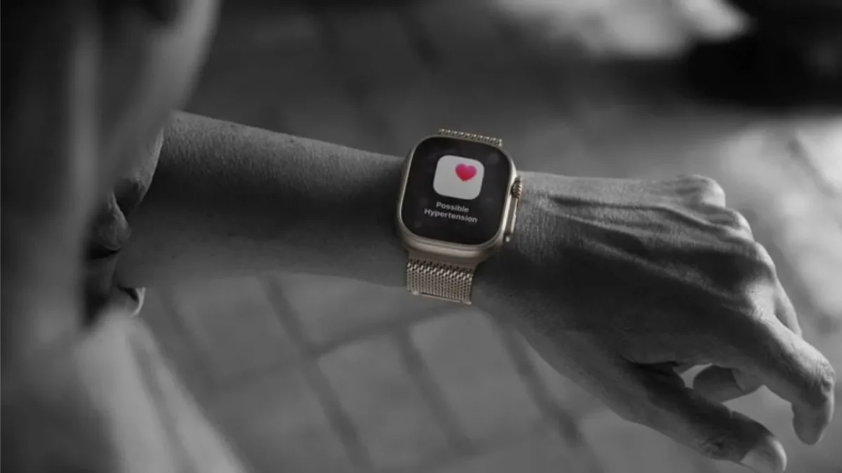 Uma pessoa olha para o seu Apple Watch, que exibe no ecrã uma notificação de saúde com o texto: 'Possível Hipertensão'.