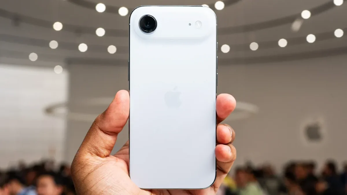 Uma pessoa a segurar um iPhone branco, mostrando a traseira do telemóvel com um novo design de câmara horizontal, num evento da Apple.