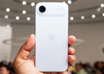 Uma pessoa a segurar um iphone branco, mostrando a traseira do telemóvel com um novo design de câmara horizontal, num evento da apple.