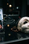 Telemóvel exibe retrato falso ao lado de máscara teatral para ilustrar a falta de transparência do selo criador de ia na rede social da meta.