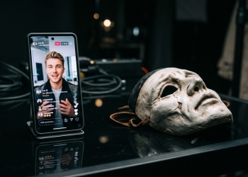 Telemóvel exibe retrato falso ao lado de máscara teatral para ilustrar a falta de transparência do selo criador de ia na rede social da meta.